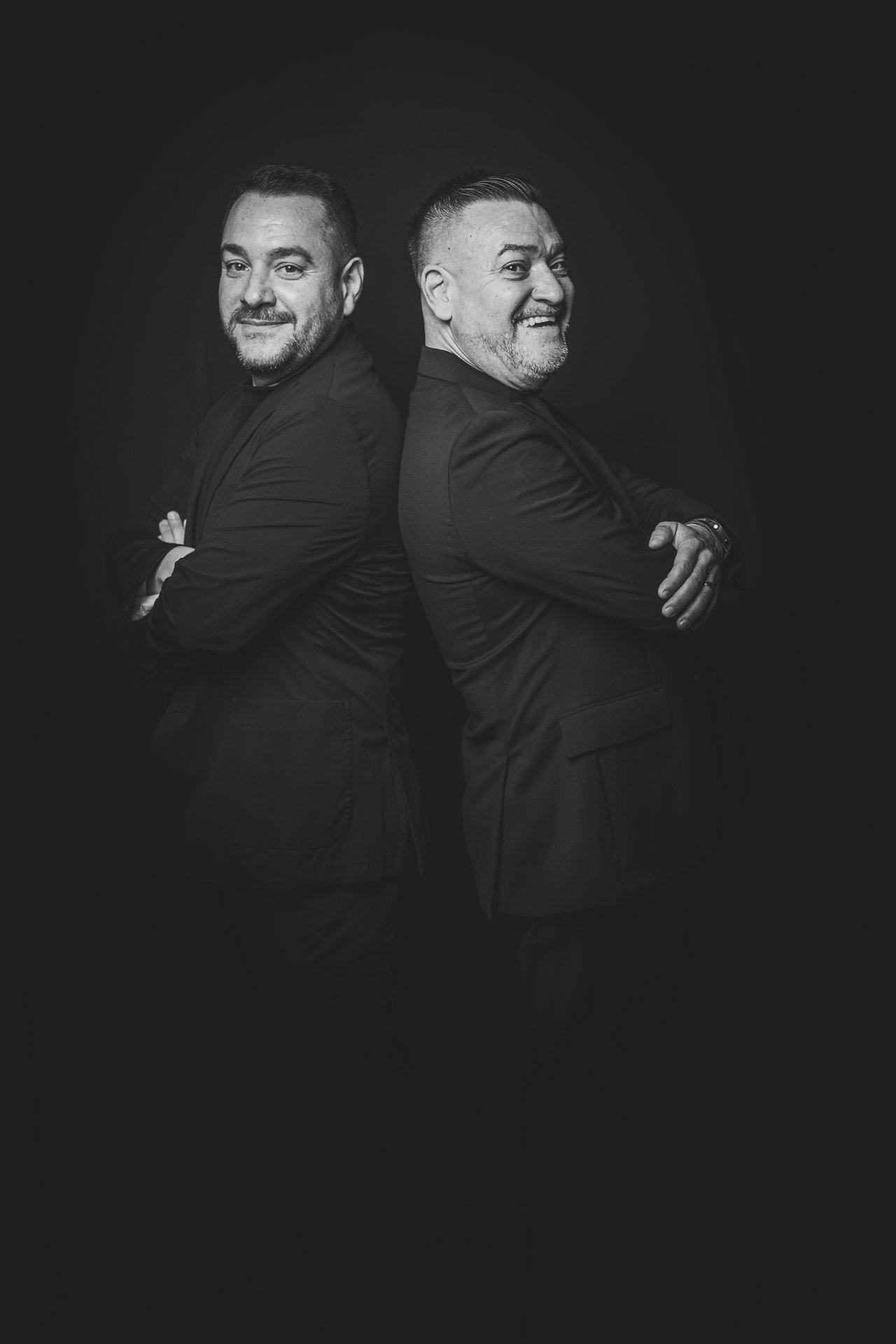 Retrato editorial de dos invitados espalda con espalda con fondo negro
