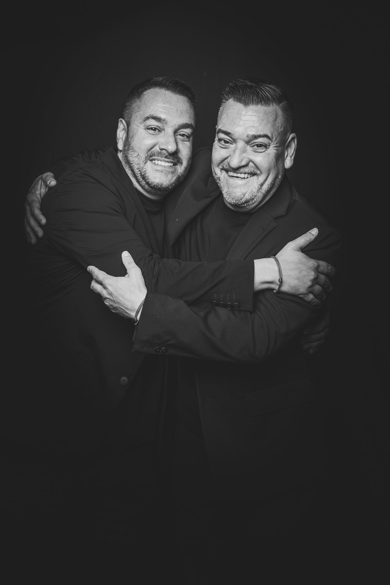 Retrato editorial de dos invitados abrazados con fondo negro
